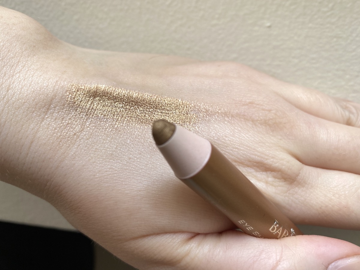 Guldskimrande ögonpenna hålls upp av en hand. 