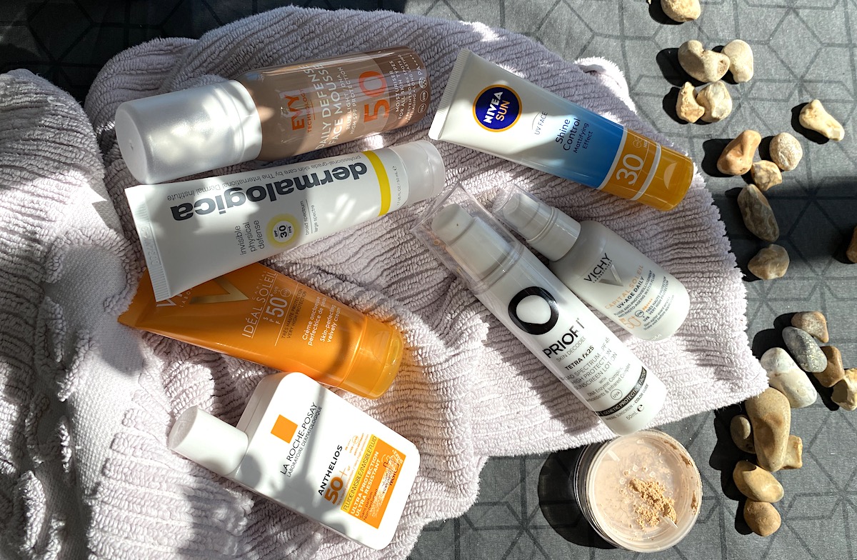 Utspridda tuber och flaskor med solprodukter ligger på en handduk. Stenar ligger vid sidan och flera produkter är skuggade. 